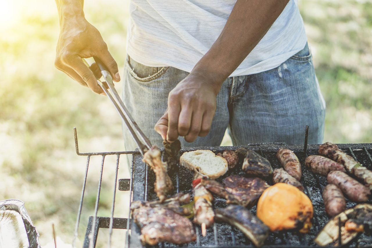 man cooking meat on barbecue chef putting some sausages on grill in park outdoor